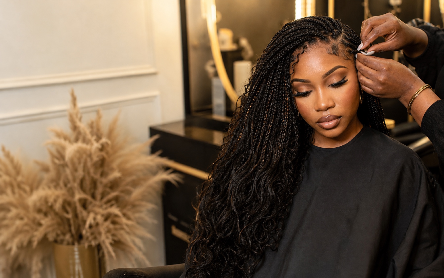 Stylist finishing long braids in a luxury black and gold salon